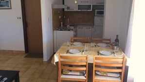 A dining area with a table set for four, wooden chairs, and a kitchen in the background. - Apartments Ognjen (Tisno)