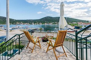 Un balcón con dos sillas y una mesa de madera, con vistas a un puerto deportivo con barcos y un paisaje montañoso.