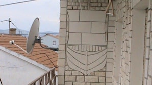 Un étroit couloir extérieur doté d’un sol carrelé, d’un mur en pierre orné de motifs décoratifs et d’une rambarde en métal.