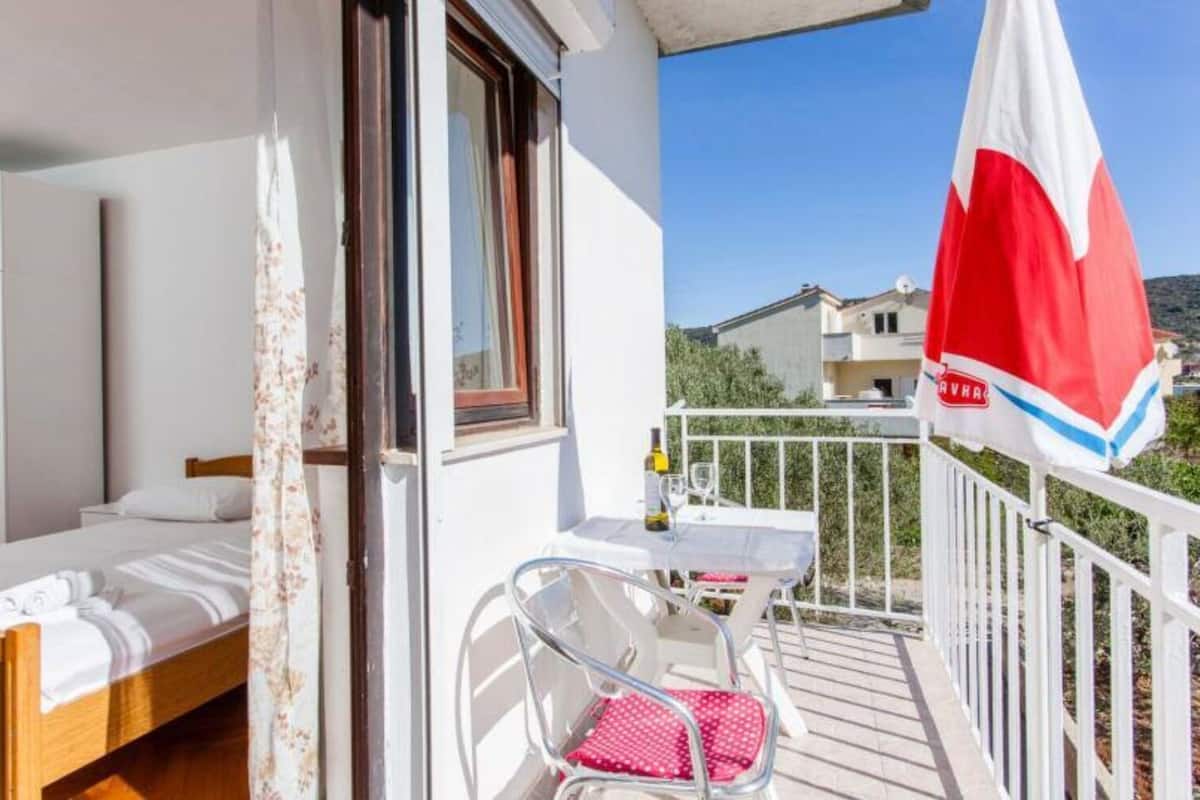 Ein Balkon mit einem Bett, einem Tisch mit einer Flasche und einem Stuhl.