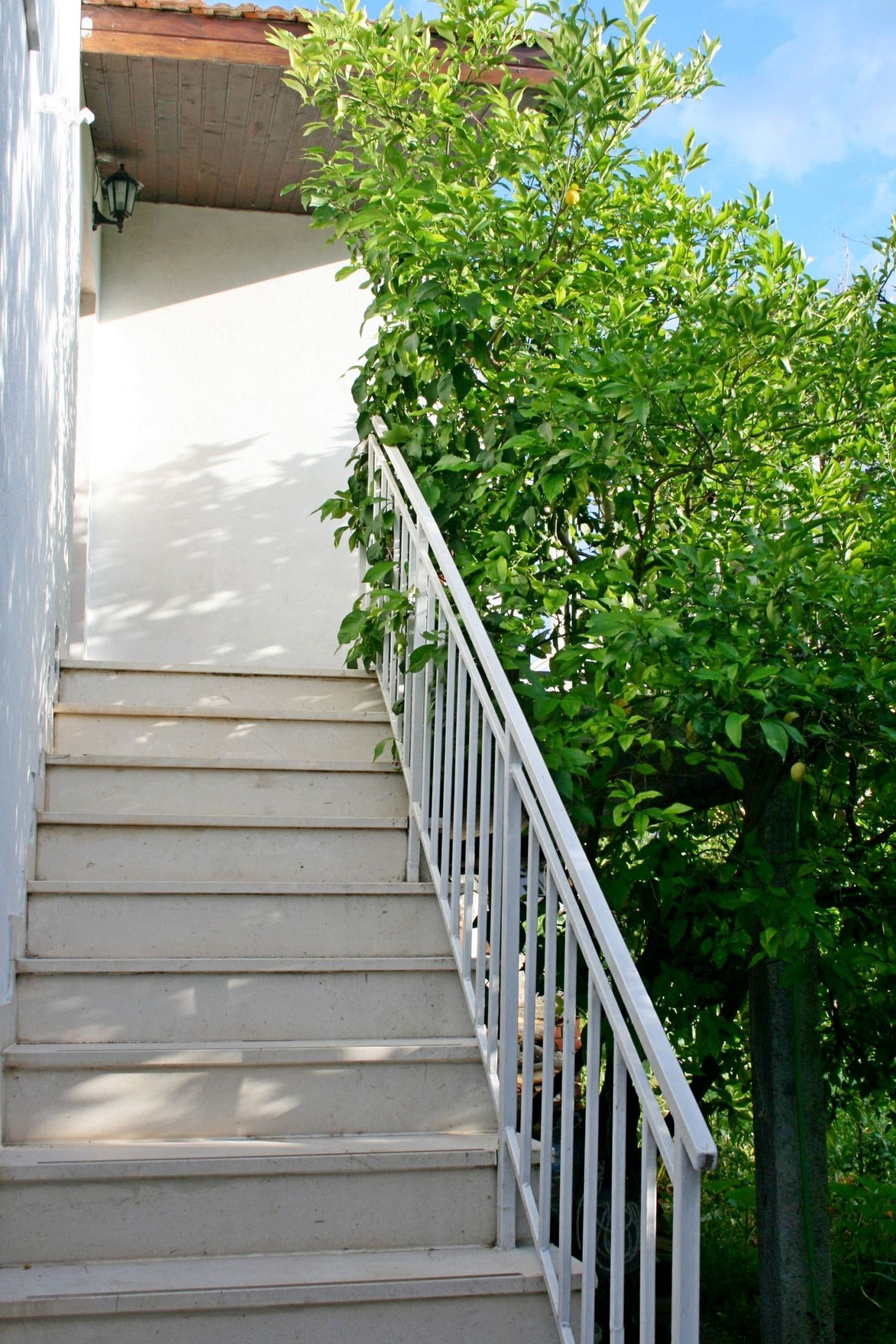 A white staircase with a metal railing, leading up to a building with a red-tiled roof.