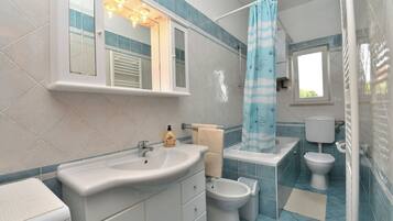 Un baño con lavamanos, espejo, toallero, inodoro y cortina de ducha.