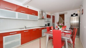 Una cucina moderna con mobili rossi e bianchi, un'area pranzo con tavolo apparecchiato per due e un frigorifero in acciaio inossidabile.