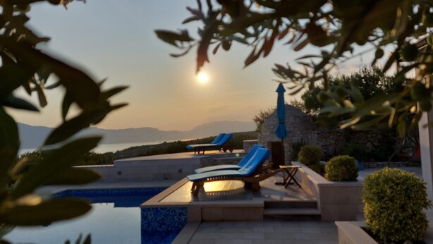 A pool area with lounge chairs and a stone structure, overlooking a body of water and distant mountains. - House Ita (Postira)