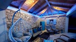 A cozy attic room with a stone wall, a hanging chair, a sofa, and a TV mounted on the wall. - House Ita (Postira)