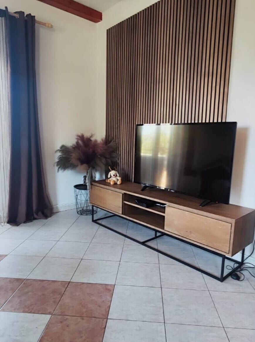 A modern living room with a TV on a wooden cabinet, a small side table with a vase, and a curtain on the left.