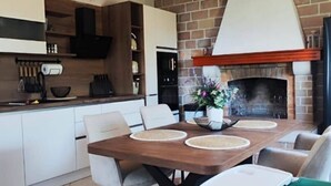 A modern kitchen with a brick fireplace, a dining table with chairs, and a kitchen counter with utensils. - House Ita (Postira)