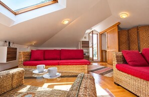 A cozy living room with a red sofa, wicker furniture, and a skylight. - Apartment Mana (Split)