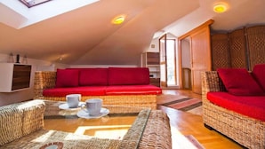 A cozy loft-style living room with a high ceiling, a red sofa, wicker furniture, and a skylight. - Apartment Mana (Split)