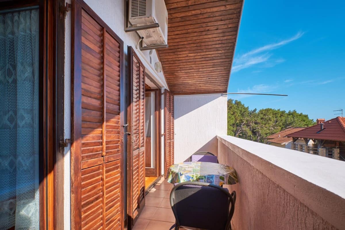 A balcony with wooden shutters, a small table, and a chair.