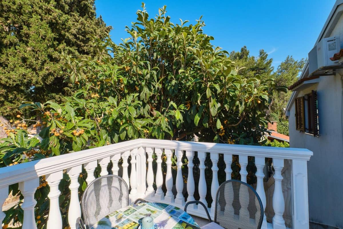 A balcony with white balustrades, two wicker chairs, and a table with a floral tablecloth.