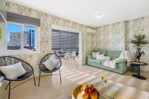 Una sala de estar con un sofá verde, sillas negras, una mesa de comedor y un amplio ventanal con persianas.