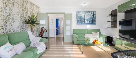 A modern living room with a green sofa, a glass coffee table, and a painting on the wall.