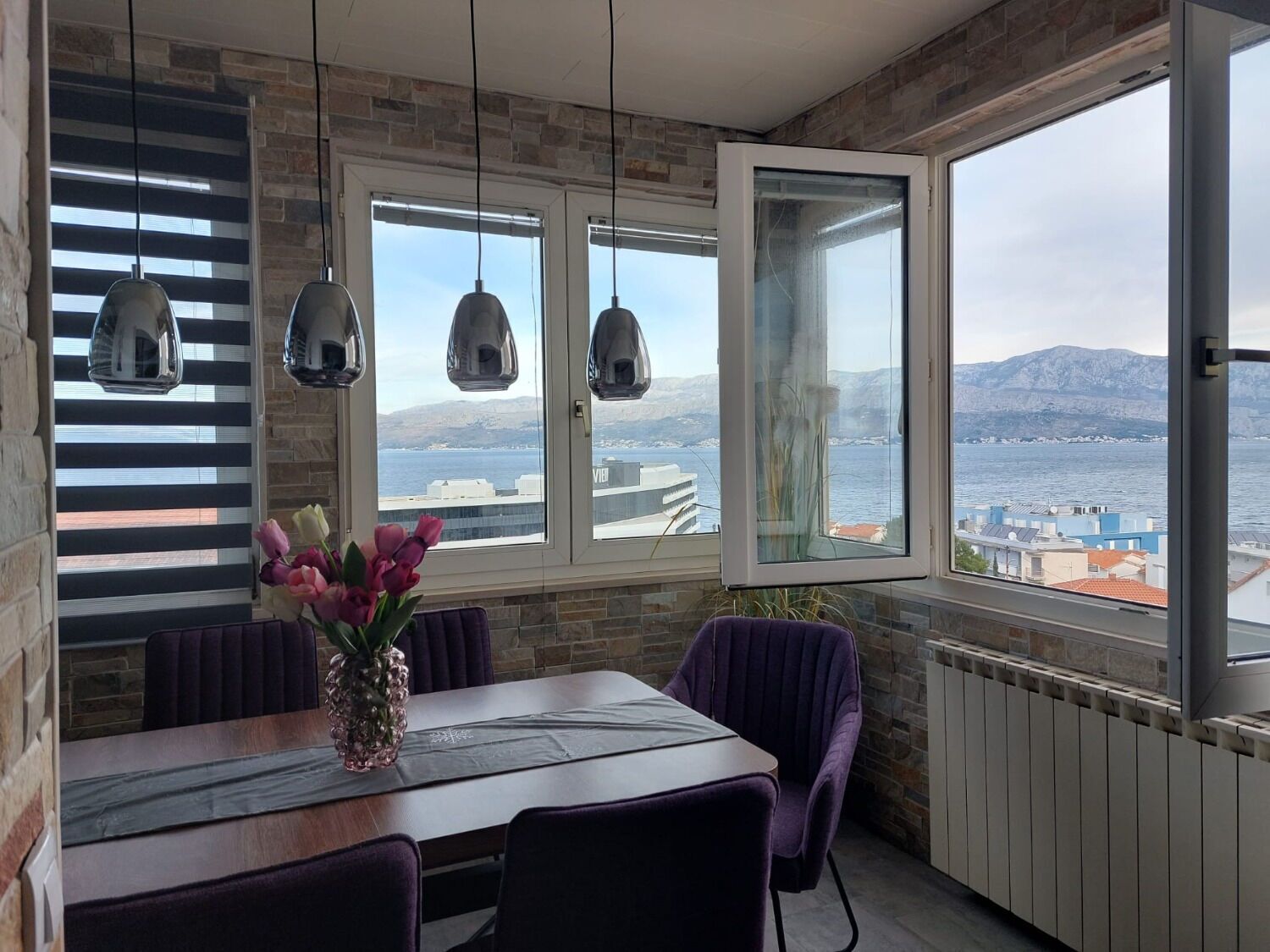Een eetgedeelte met een tafel, stoelen en uitzicht op zee en bergen.