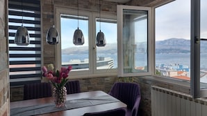 A dining area with a table, chairs, and a view of the sea and mountains. - Apartments Ita 1 (Postira)