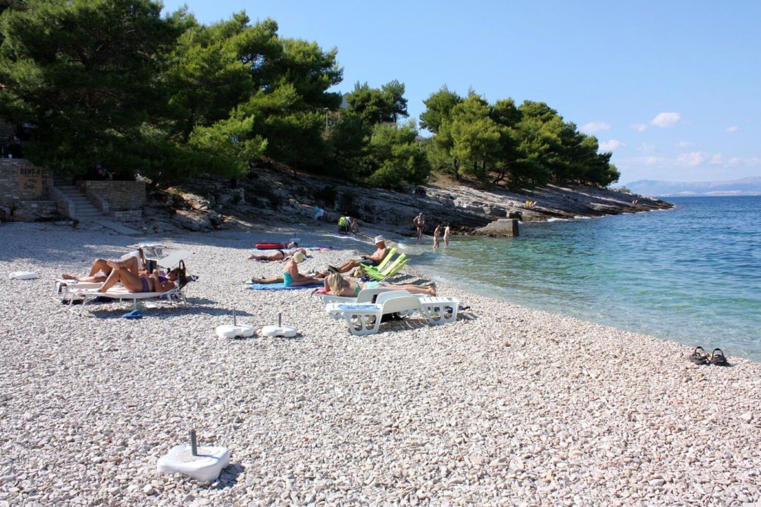 Una spiaggia ciottolosa con persone che prendono il sole e nuotano.