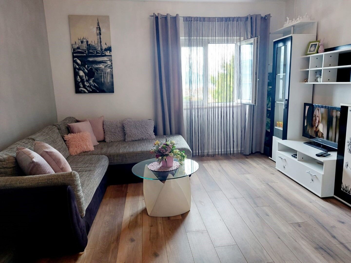 A living room with a sofa, a glass coffee table, a TV, and a painting on the wall.
