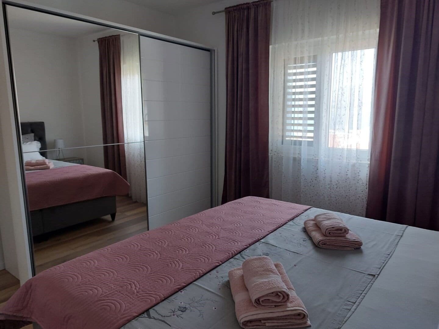 A bedroom with a bed, a mirror, a wardrobe, and a window with curtains.