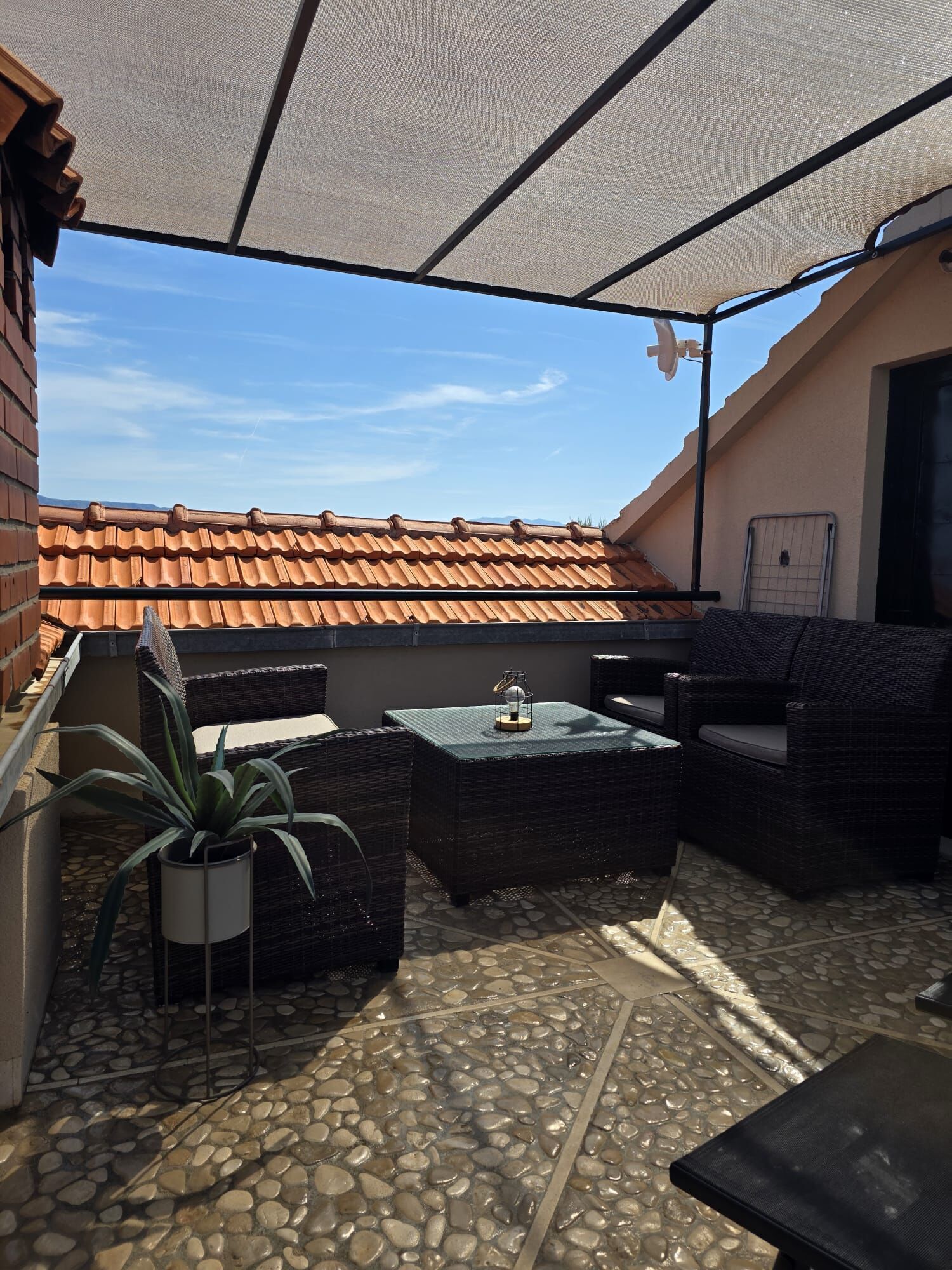 Un patio cubierto con mobiliario de mimbre, una planta en maceta y suelo de baldosas.