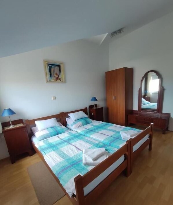 A bedroom with a wooden bed, a wardrobe, a nightstand with a lamp, and a painting on the wall. - Apartments Antonija (Marina)