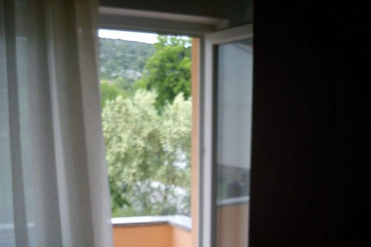 A balcony with a chair, a view of greenery, and a door leading to an interior space.