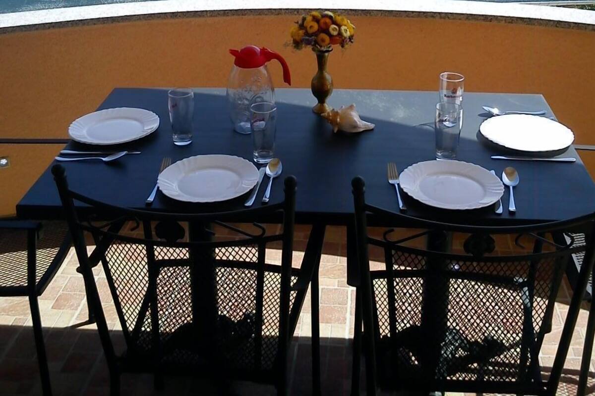 A dining table set outdoors with a view of a white building with a red-tiled roof.
