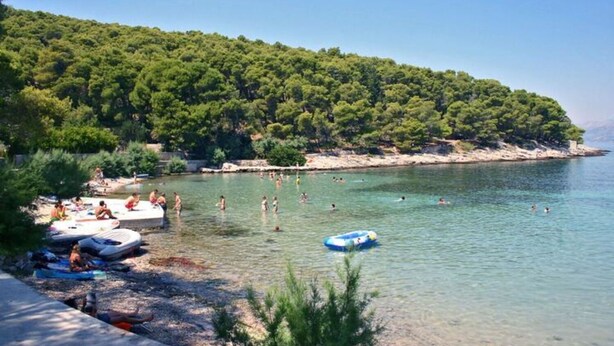 A beach with clear waters, people swimming and sunbathing, and boats on the shore. - Apartment Elena (Postira)