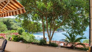 A balcony with a view of the sea, a chair, and a striped umbrella. - Apartment Elena (Postira)
