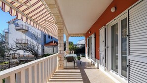 A covered outdoor area with a tiled floor, a table with chairs, and a view of a building with balconies. - House Vesnad (Seget)