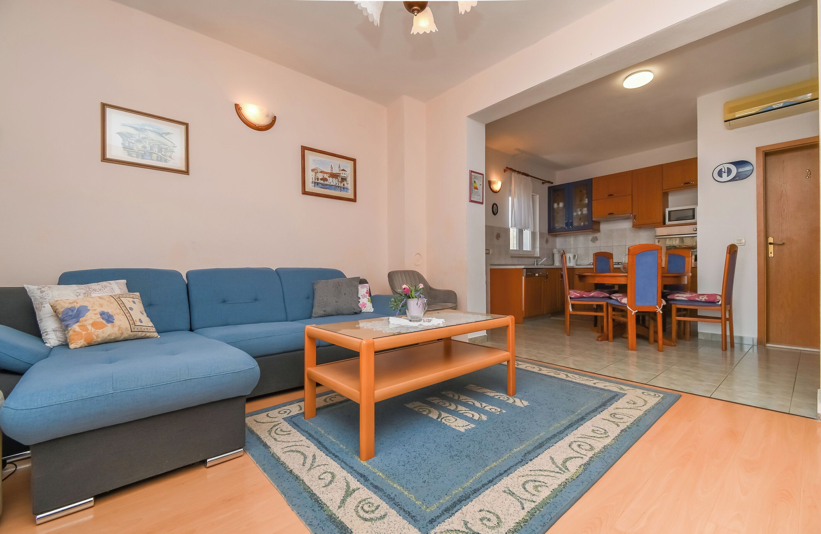 A living room with a blue sofa, a wooden coffee table, and a kitchen area in the background.
