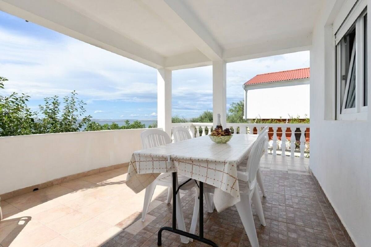 A covered outdoor patio with a table set for two, a bowl of fruit, and a view of the sea.
