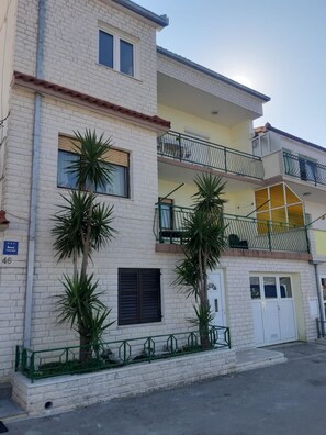 A two-story building with a brick facade, balconies, and a small garden area with palm trees. - Apartment Daria Jure (Trogir)