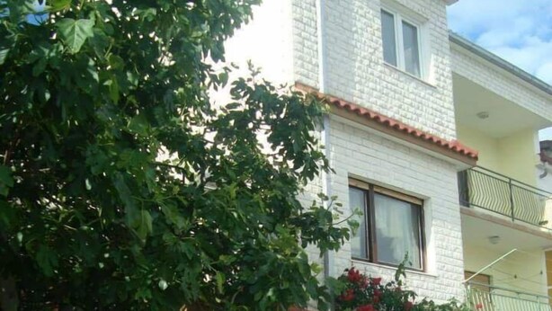 Un edificio de dos pisos con fachada de ladrillo blanco, un balcón en el nivel superior y una verja metálica verde en la entrada.