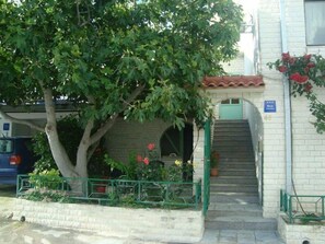 A building with a staircase leading to an entrance, surrounded by greenery and a tree. - Apartment Daria Jure (Trogir)