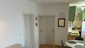 A compact living space with a dining area, a sofa, and a kitchen with a clock and green cabinets. - Apartment Dino (Supetar)