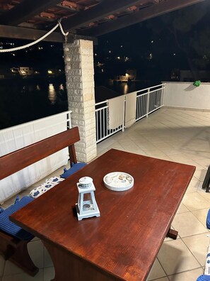 Un tavolo di legno con una lanterna e un piatto di pietre su un balcone con vista su un corpo d'acqua di notte.