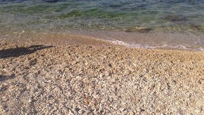 A pebbled beach with clear water and a distant shoreline. - Apartment Dino (Supetar)