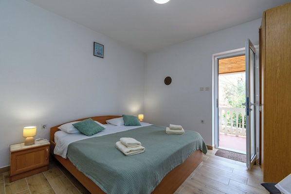 Une chambre à coucher comprenant un lit, des lampes de chevet, une porte donnant sur un espace extérieur et un petit tableau accroché au mur.