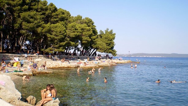 Egy strand, ahol az emberek úsznak és pihennek, melyet fák és sziklás képződmények vesznek körül.