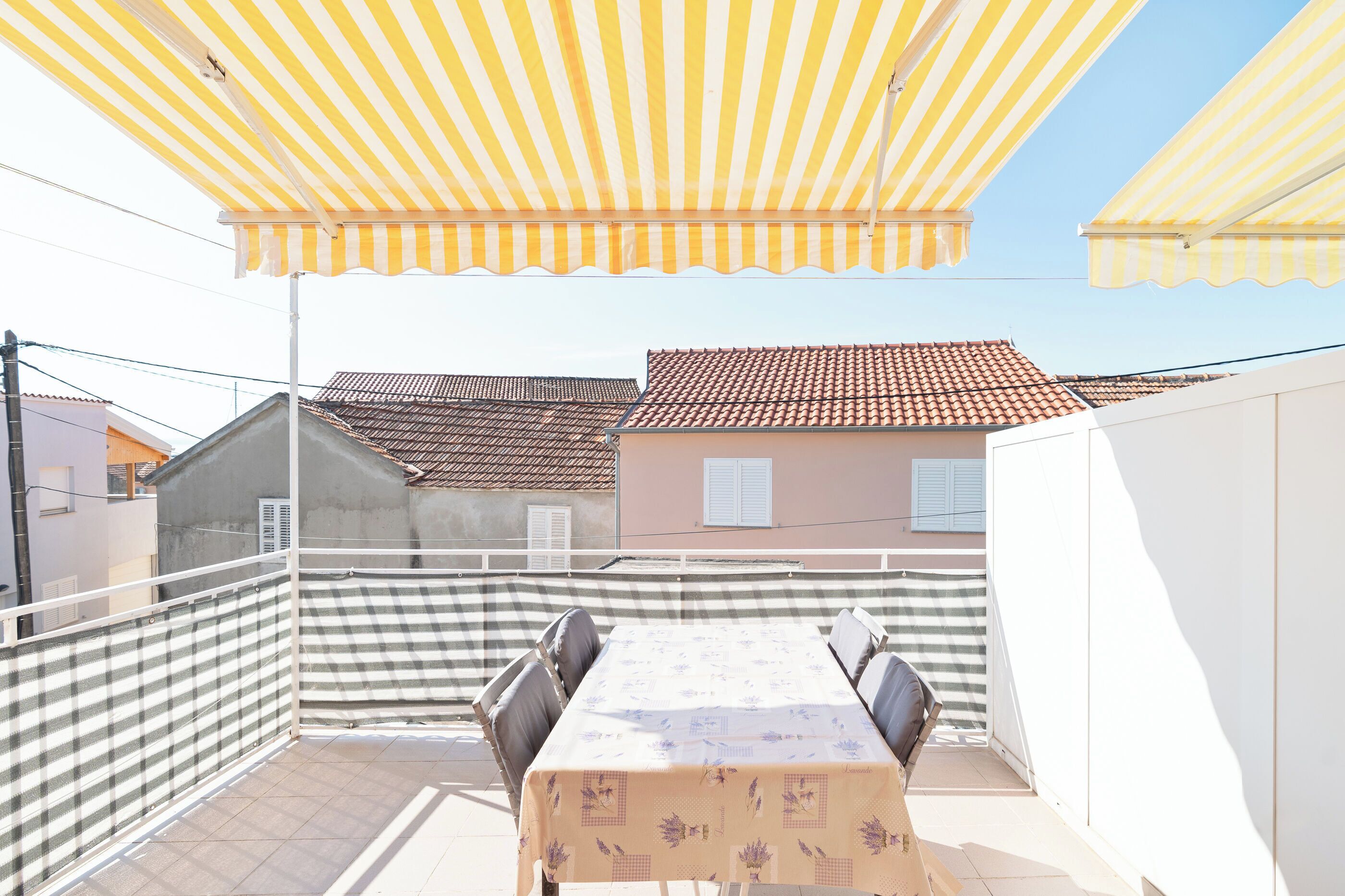 A balcony with a checkered fence, a table with chairs, and a yellow striped awning.