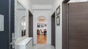A hallway with a white tiled floor, a dark wooden door, and a white console table with a mirror. - Apartment Vlatkica (Jasenice)