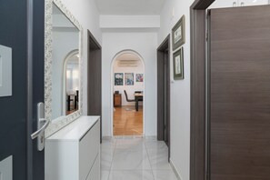 A hallway with a white tiled floor, a dark wooden door, and a white console table with a mirror. - Apartment Vlatkica (Jasenice)