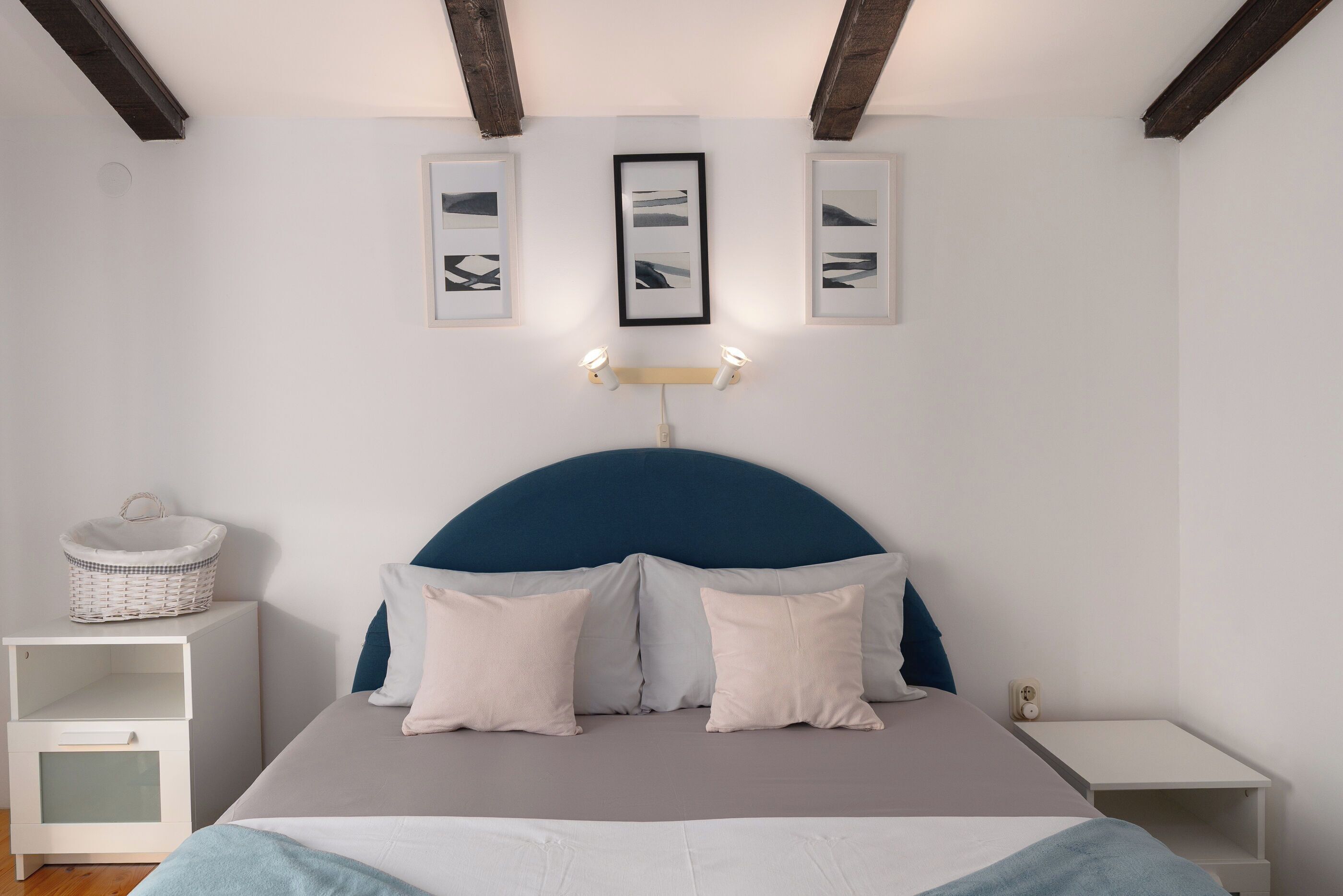 A bedroom with a bed, bedside tables, a headboard, wall-mounted light fixtures, and framed pictures.
