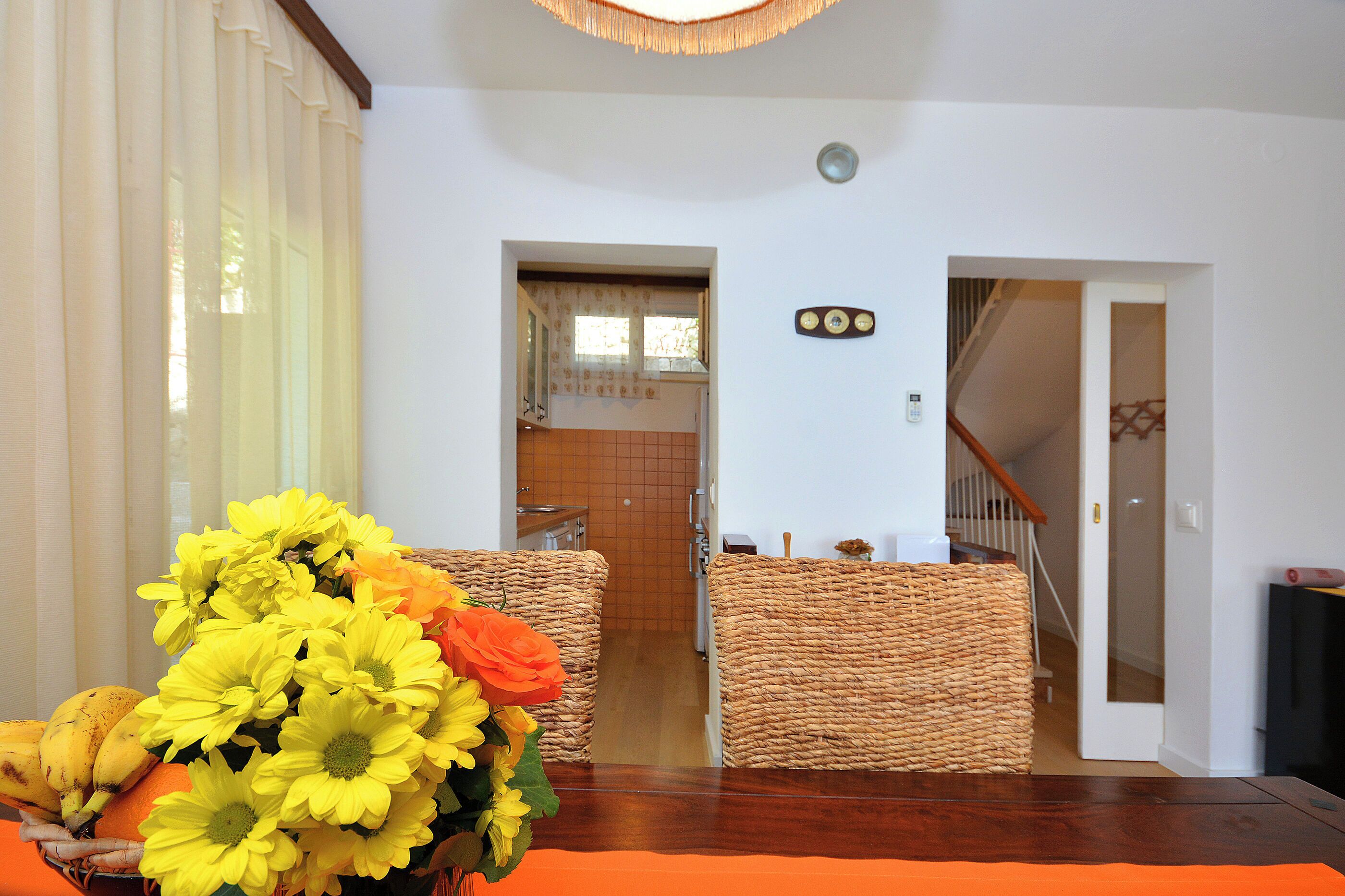 A room with a wooden floor, a dining table with a vase of flowers, and a staircase leading to another room.