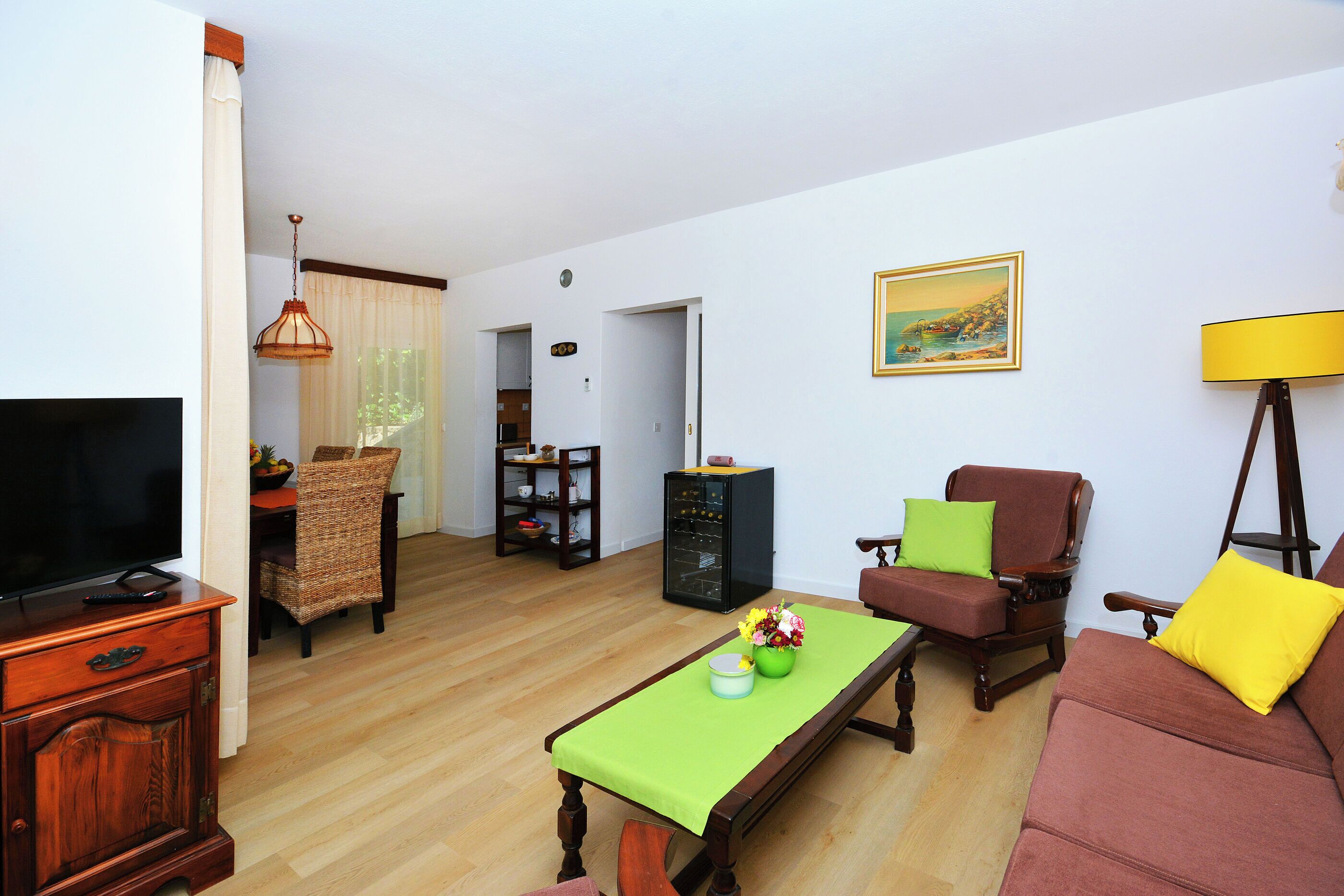 A living room with a television, a sofa, a dining table, and a bookshelf.