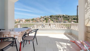 A balcony with a view of a hillside town, a table with chairs, and a striped rug. - Apartments Gogi (Postira)