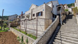 A residential building with a stone facade, a balcony, and a staircase leading up to the entrance. - Apartments Gogi (Postira)