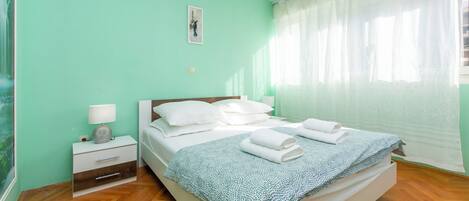 Una camera da letto con un letto, un comodino, una lampada e una finestra con tende leggere.