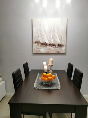 A dining table with a centerpiece of oranges and candles, surrounded by black chairs, with a sailboat painting on the wall above. - Apartment Jozo (Omis)