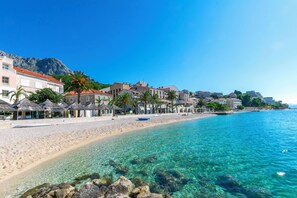 A coastal hotel with a beach view, clear blue water, and a mountainous backdrop. - Apartment Livr (Podgora)